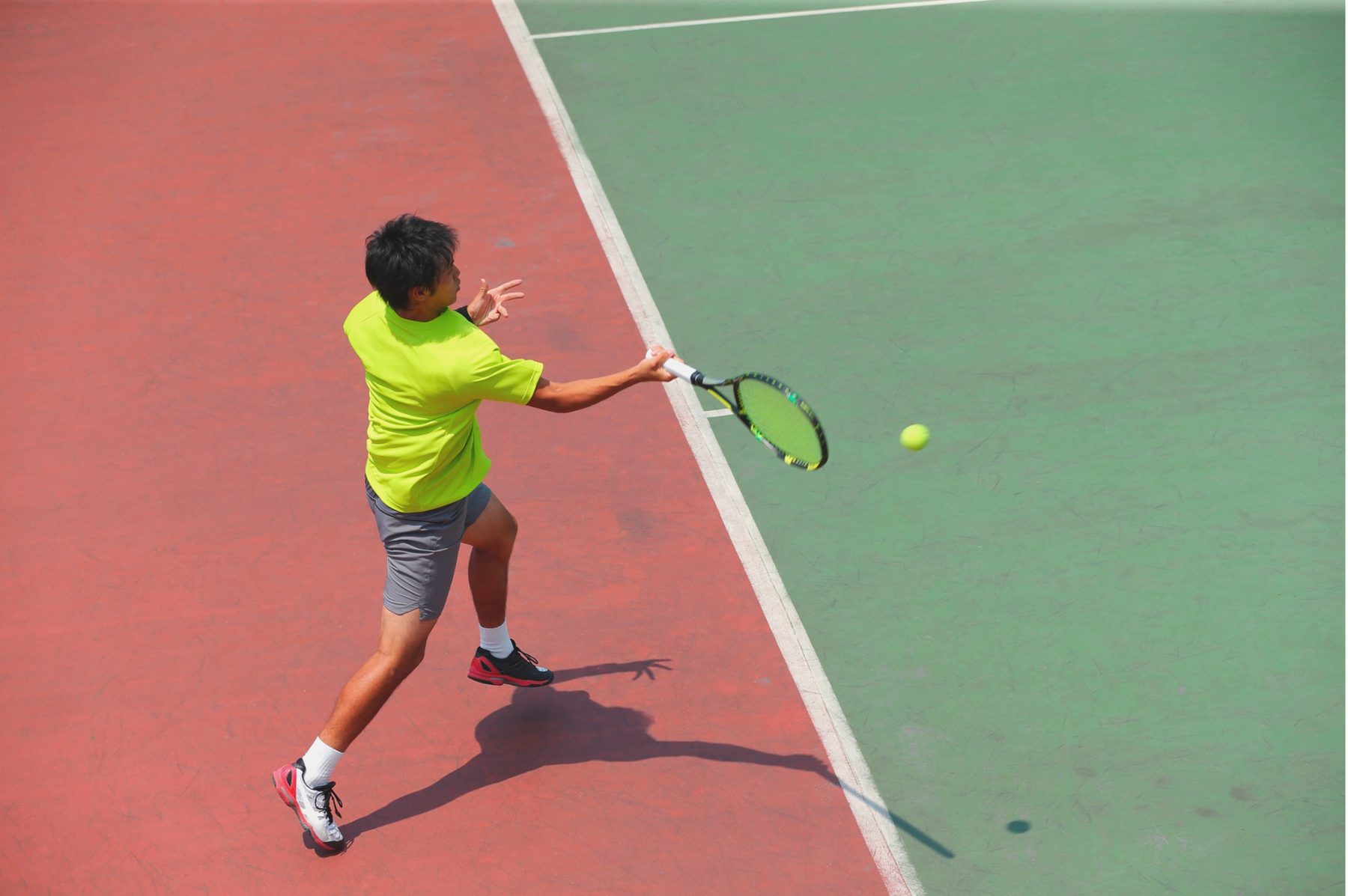 A player hitting a forehand where a clay-red court meets a green one